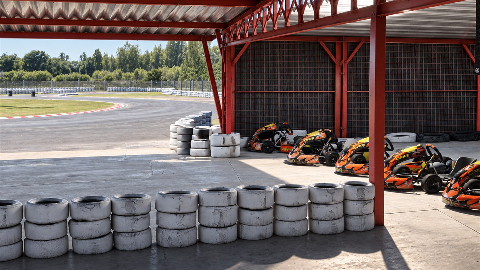 Karts estacionados bajo la estructura roja de boxes, junto a barreras de neumáticos.